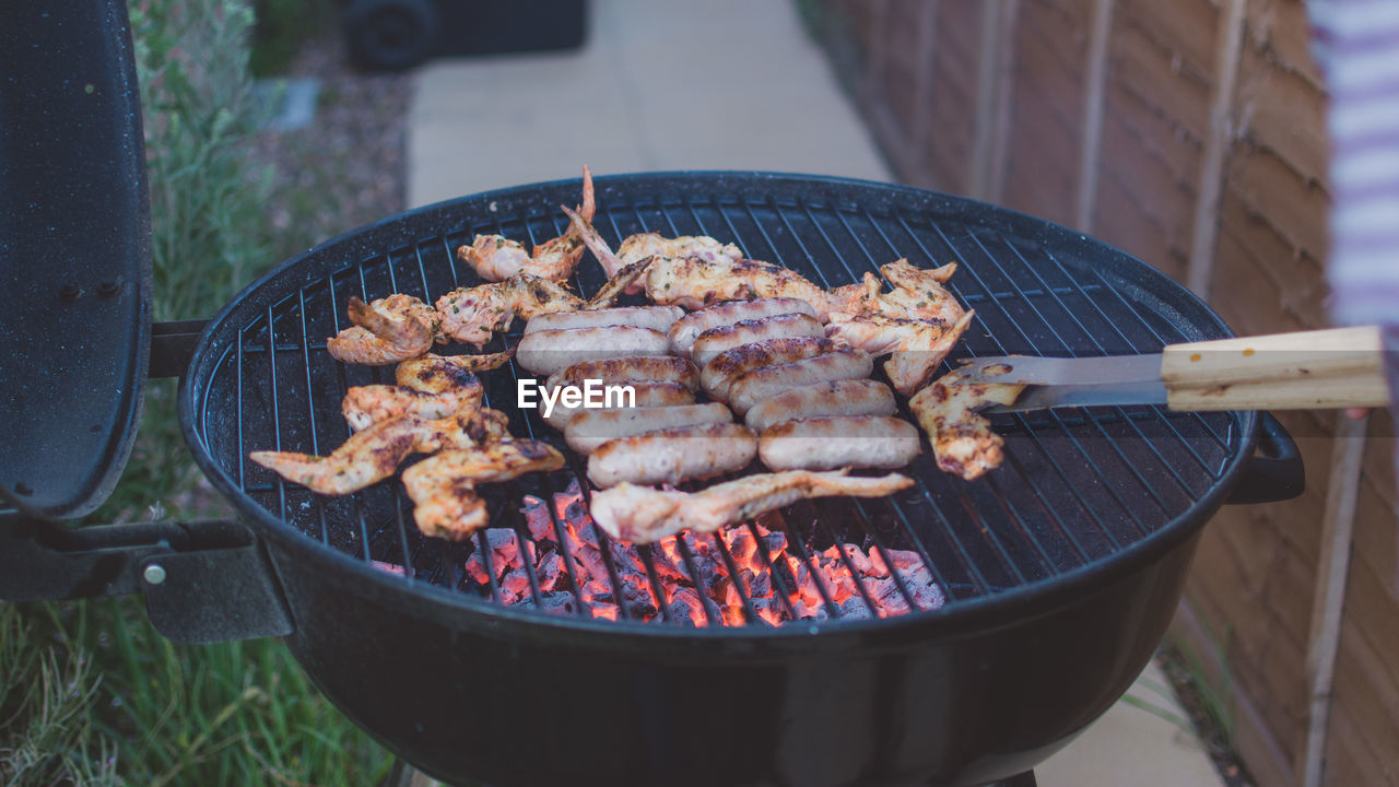 High angle view of chicken wings and sausages on barbecue grill