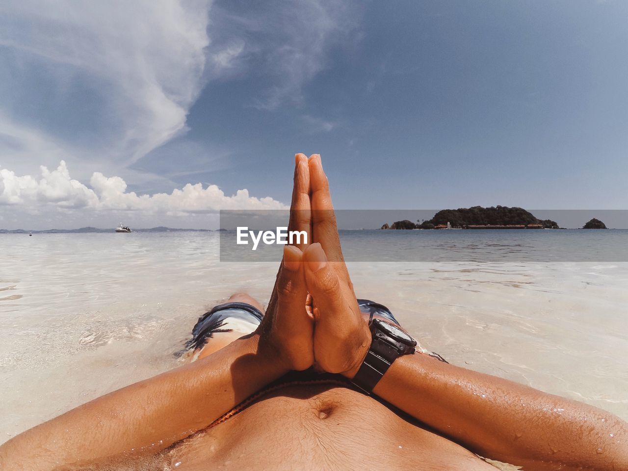 Midsection of man with hands clasped lying on shore at beach against sky