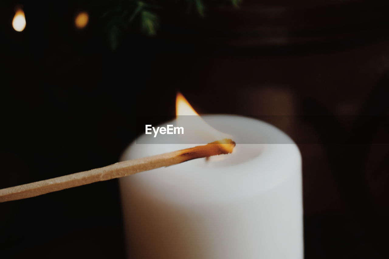 Close-up of illuminated matchstick with candle