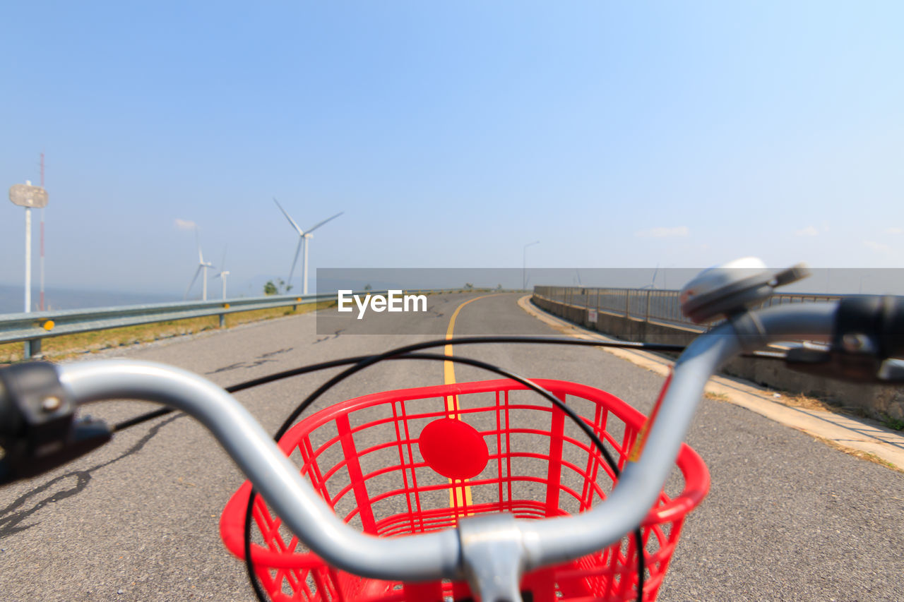 Close-up of bicycle with red basket on road against blue sky