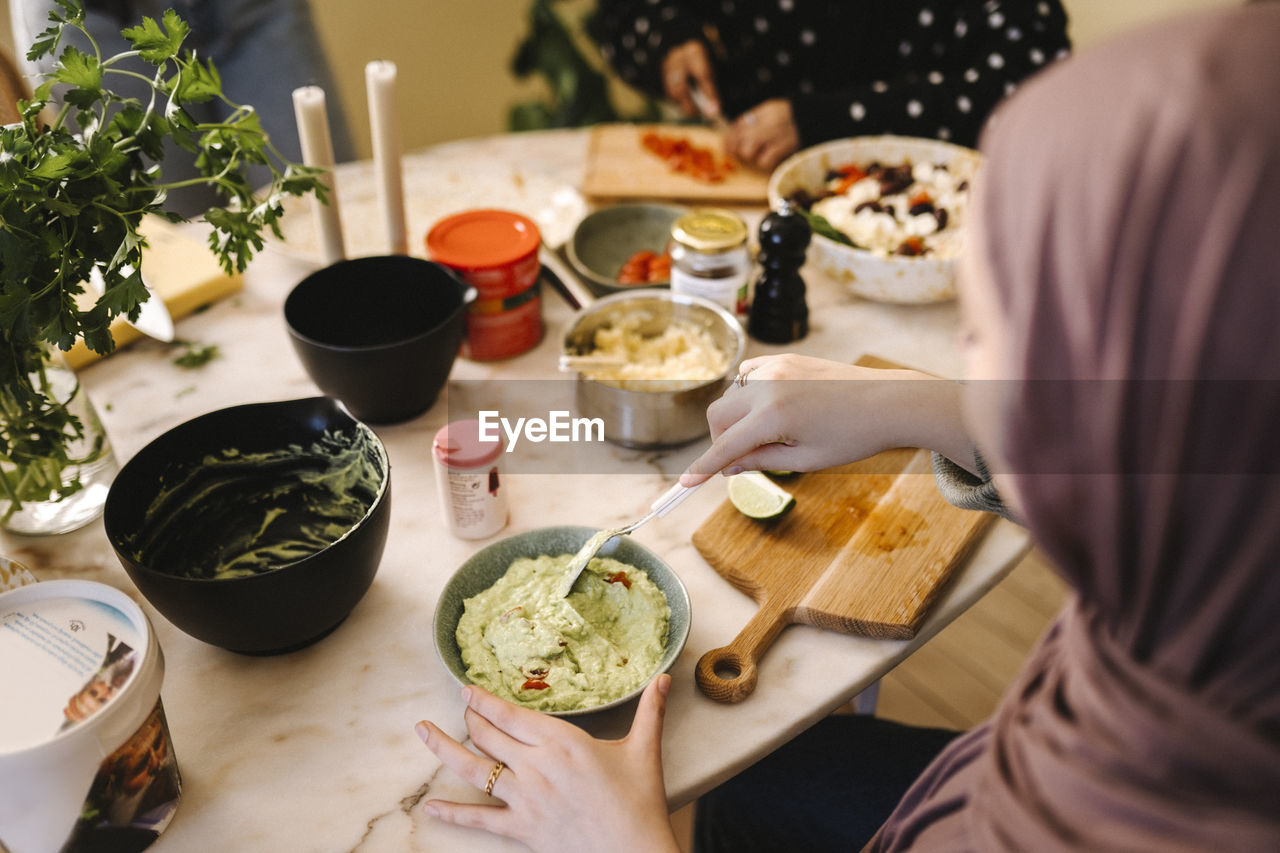 Young woman mixing dipping sauce while preparing food with friends at table