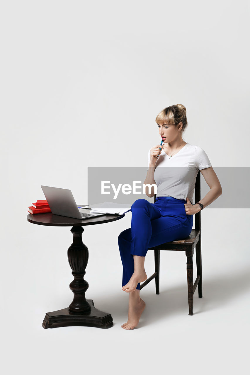 side view of woman sitting on chair against white background