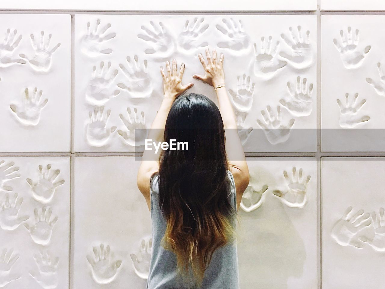 Rear view of woman touching white wall with handprints