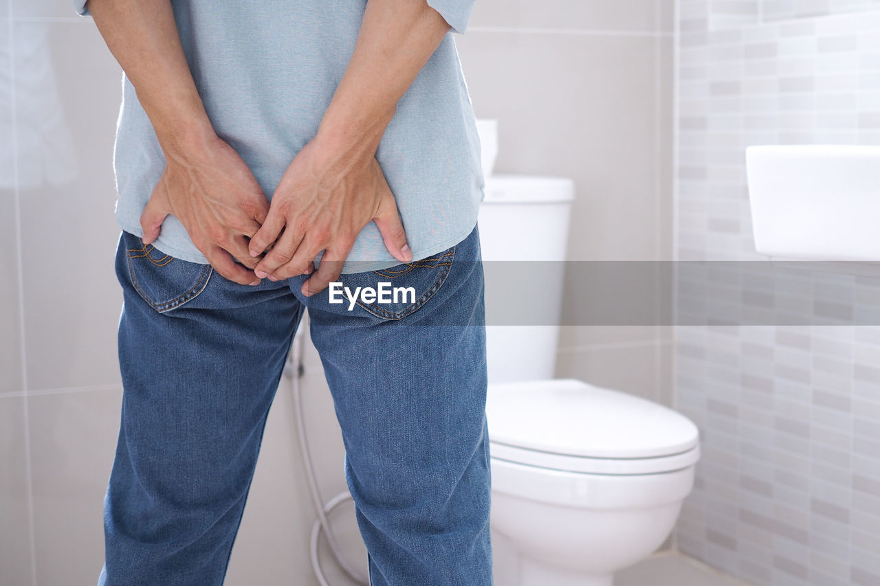 Midsection of man touching buttocks in bathroom