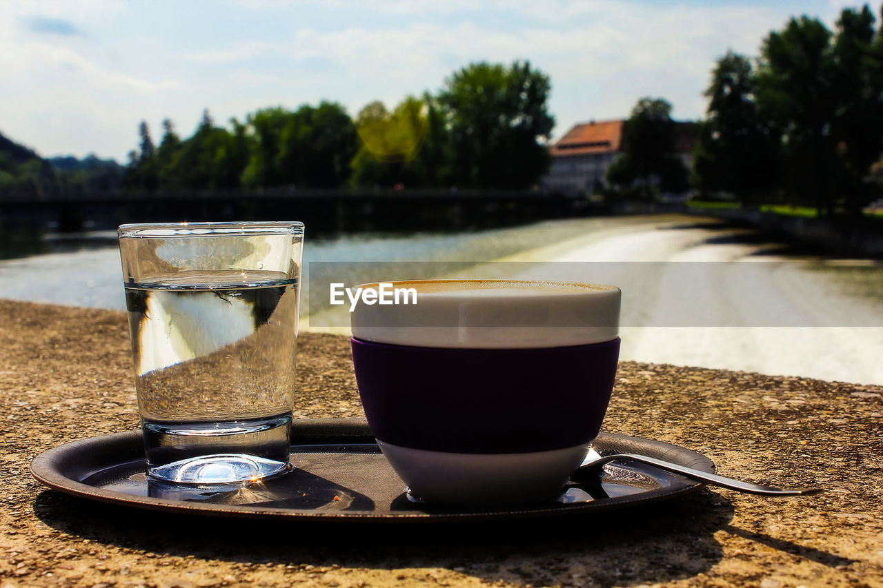 CLOSE-UP OF COFFEE CUP ON TABLE AGAINST TREES