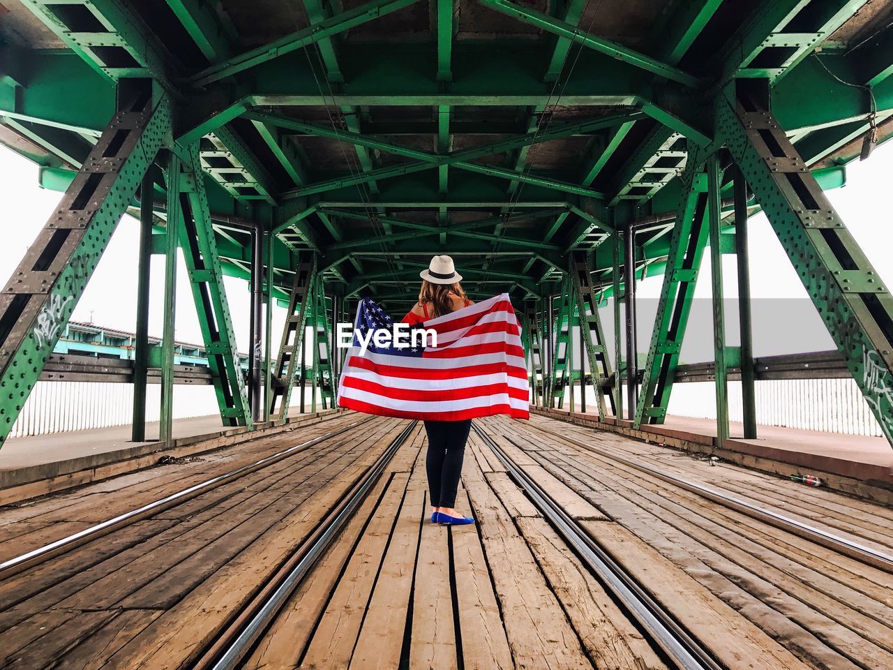 Woman holding american flag while standing on bridge