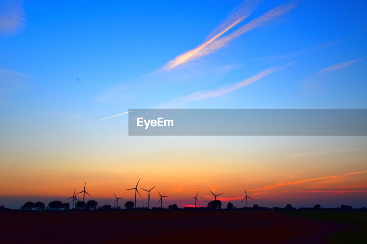 SILHOUETTE WIND TURBINES ON LAND AGAINST SKY DURING SUNSET
