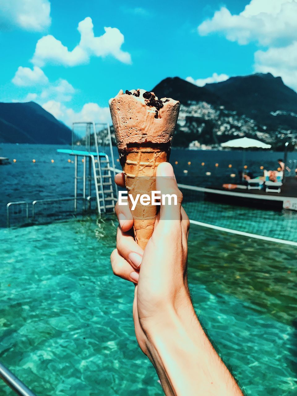 Close-up of hand holding ice cream against swimming pool