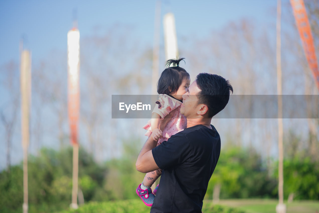 Father carrying daughter while standing in park