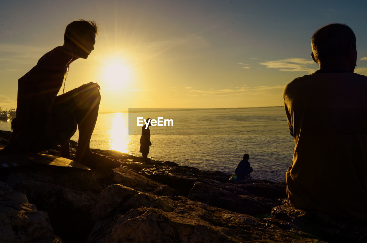 Silhouette people on rocks at beach against sky during sunset