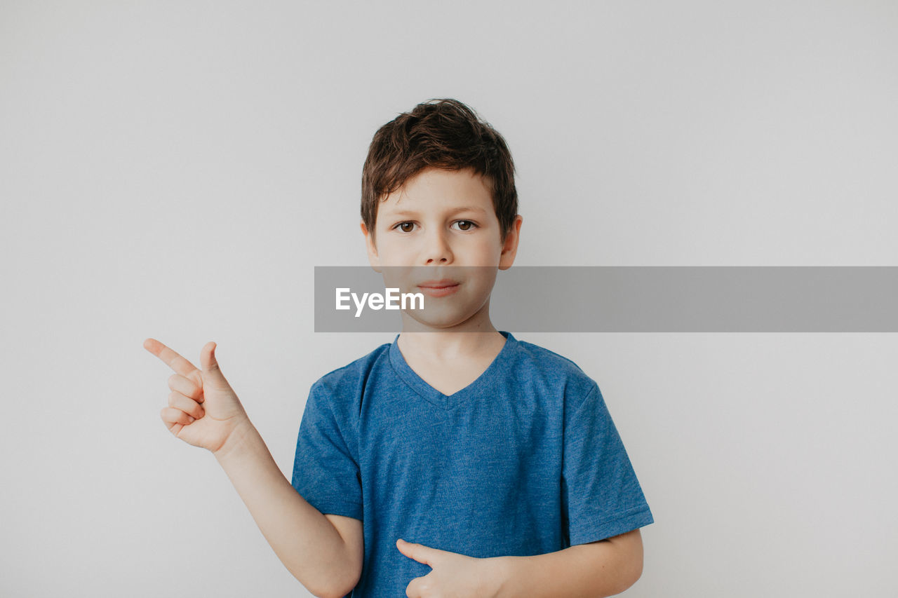 A preschool boy in a blue t-shirt on a light background shows a thumbs up. high quality photo