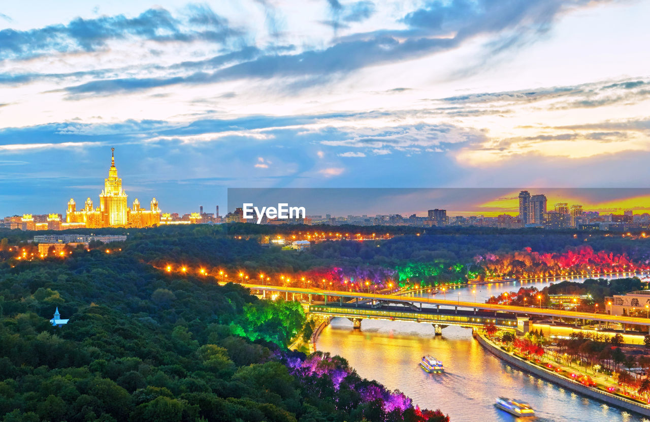 Sunset panorama with river, illuminated bridge, tourist boats and moscow university