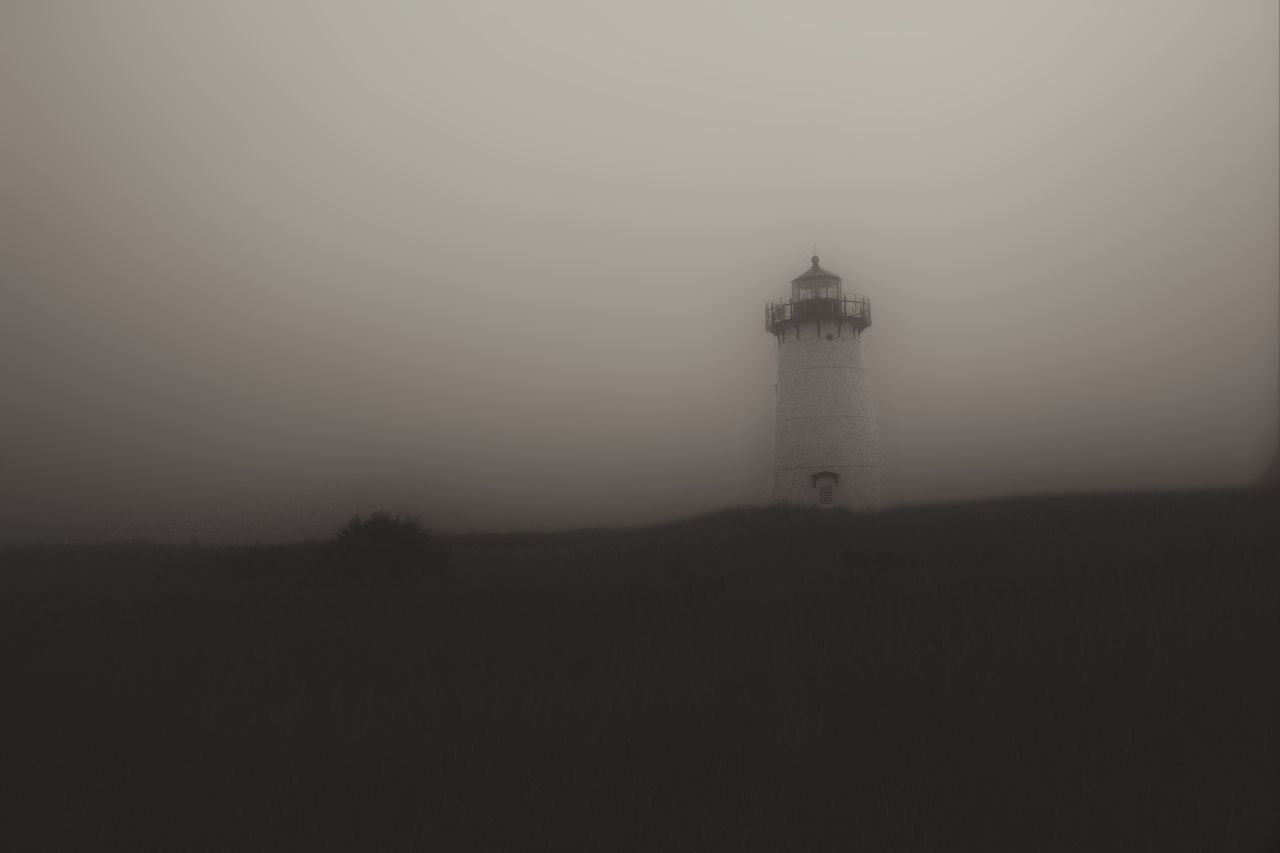 Lighthouse on silhouette field against clear sky during foggy weather