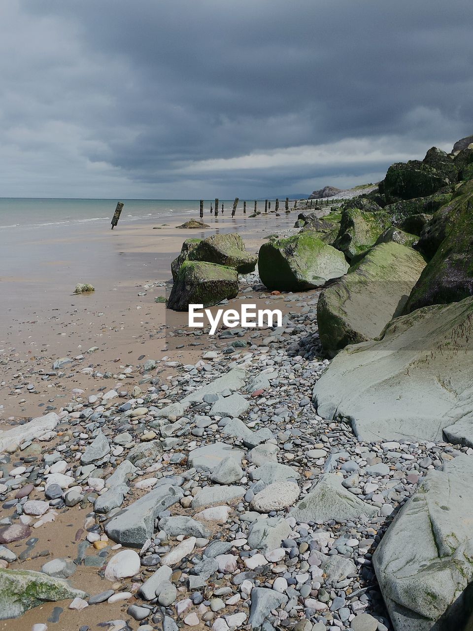 Scenic view of beach by rocks against cloudy sky