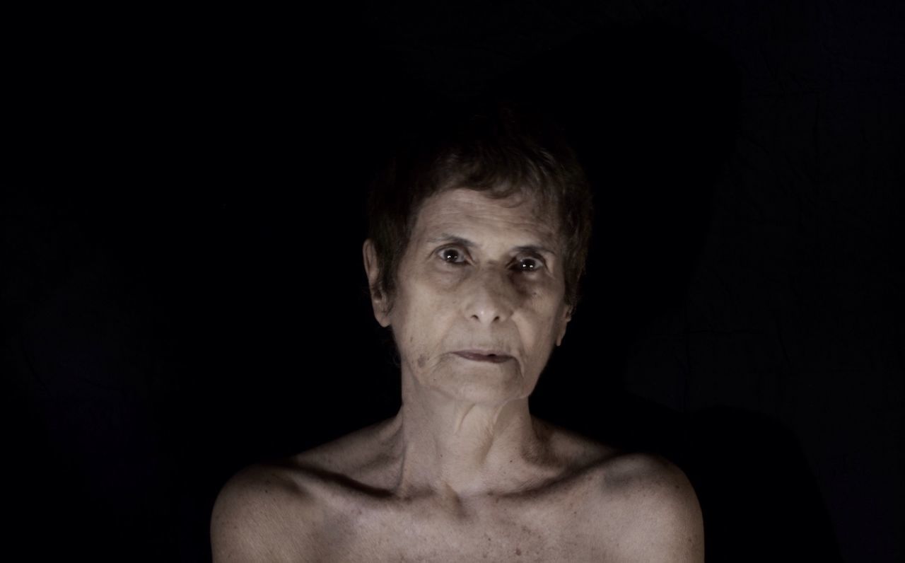 Portrait of naked woman against black background