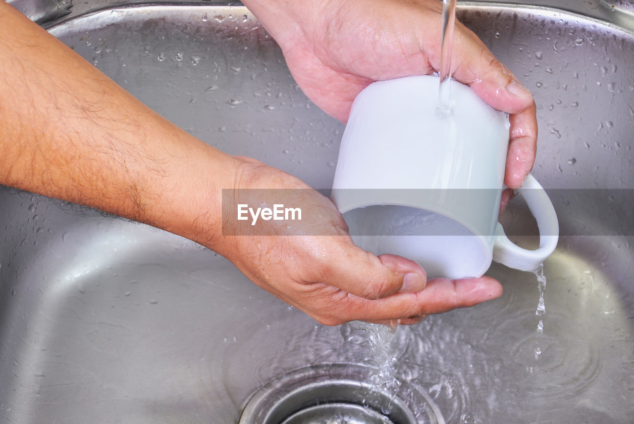 Cropped image of hands cleaning coffee cup in kitchen sink