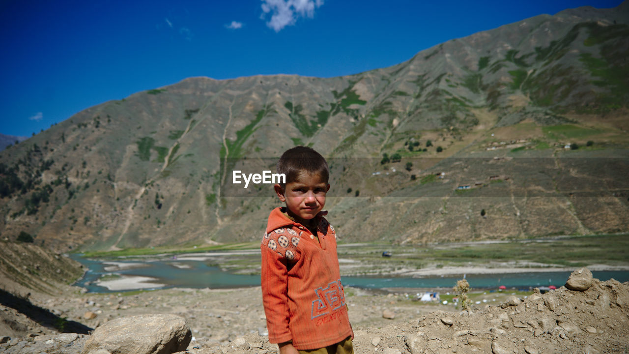 PORTRAIT OF MAN STANDING ON MOUNTAIN AGAINST SKY