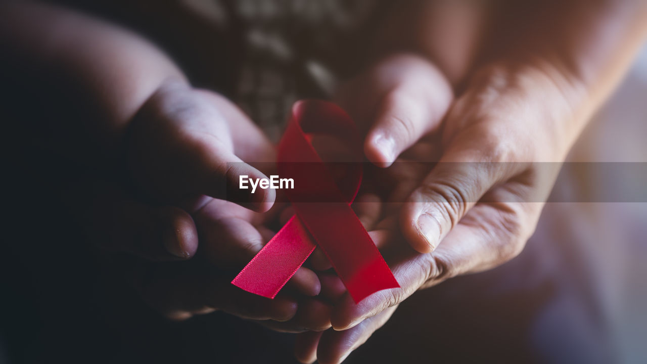 Adult and child hands holding red ribbon, hiv awareness concept, world aids day, world cancer day