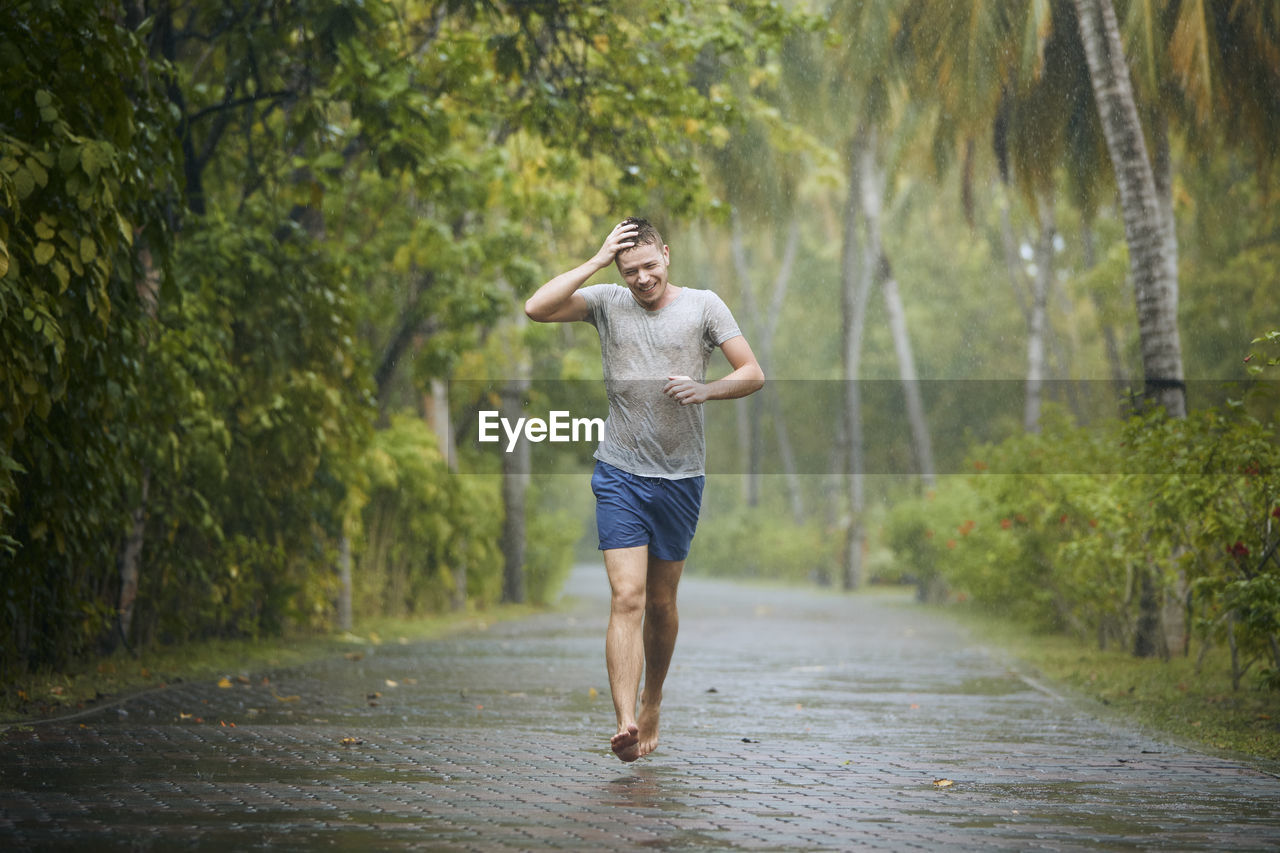 Drenched young man runing on road in heavy rain.