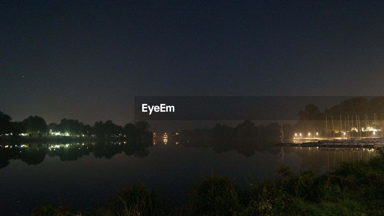 REFLECTION OF ILLUMINATED TREES IN CALM LAKE