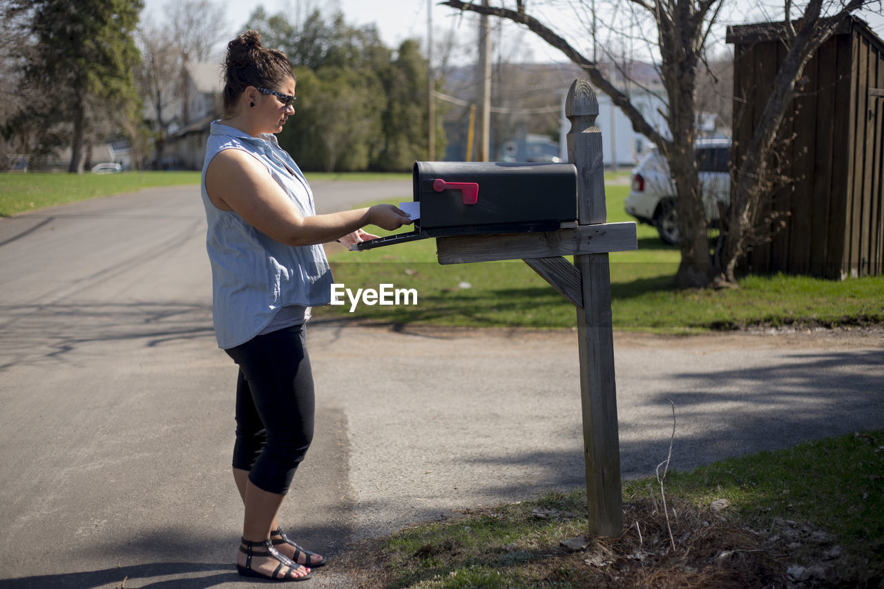 Side view of young woman standing by mailbox on street