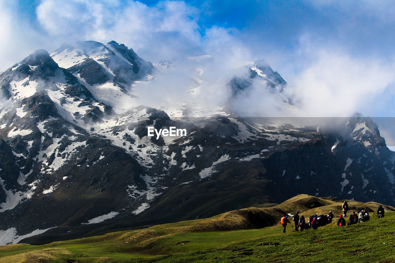 PEOPLE WALKING ON SNOWCAPPED MOUNTAINS AGAINST SKY