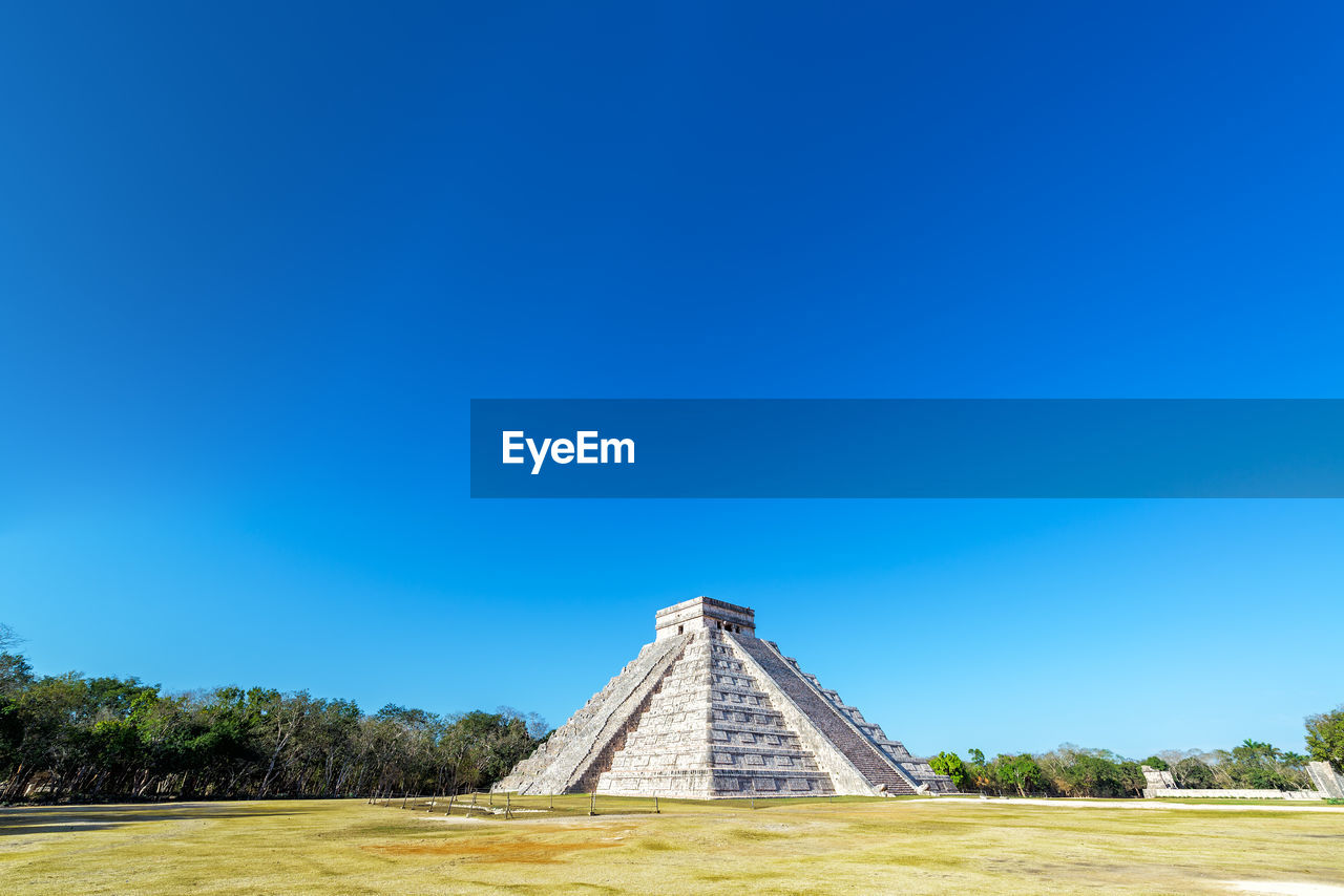 Low angle view of kukulkan pyramid against blue sky during sunny day