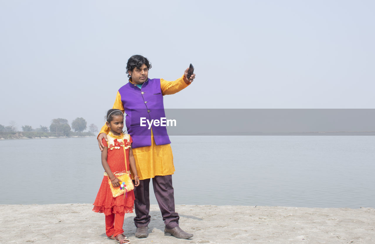 Full length of father pointing at sea while standing with daughter