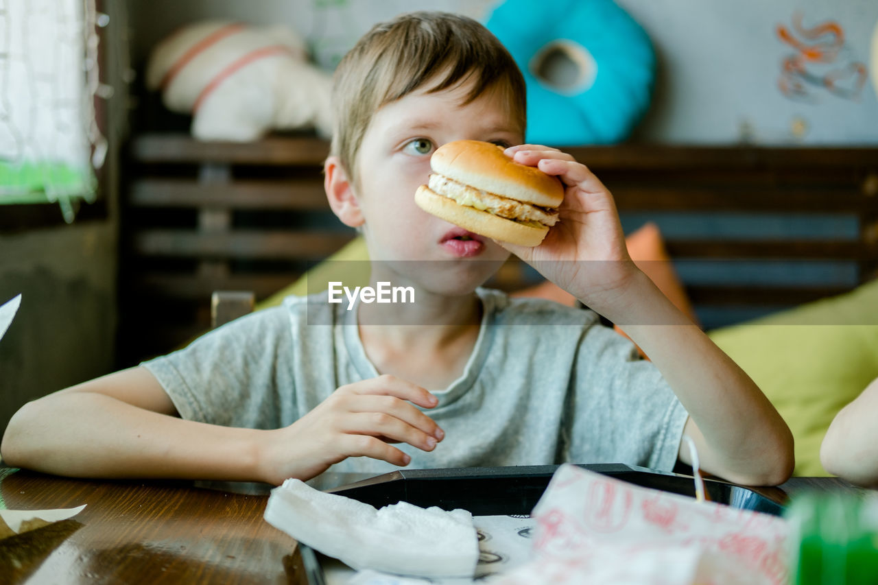 Boy eating a big burger with a cutlet. hamburger in the hands of a child. delicious chicken burger. 