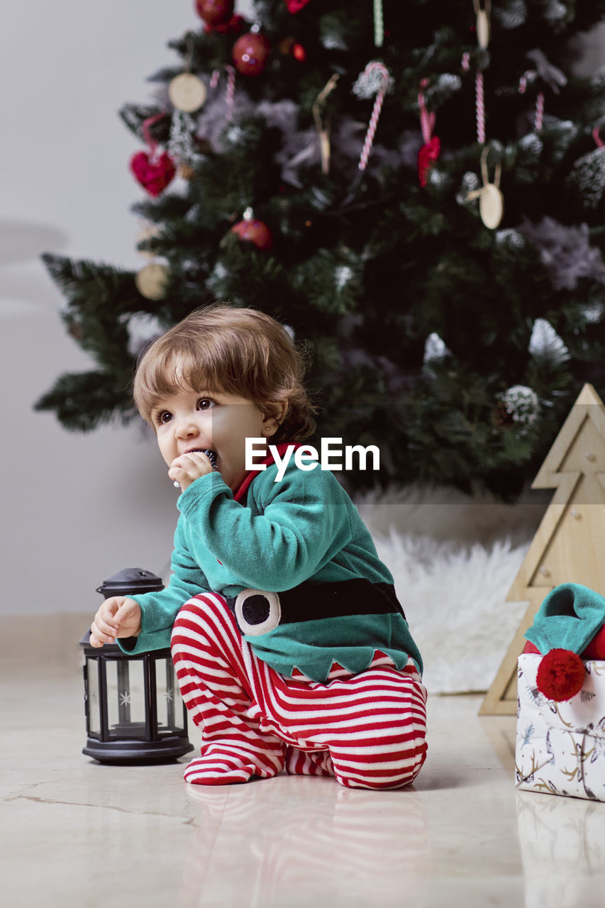 A little 12-month-old christmas elf with a christmas tree and gifts