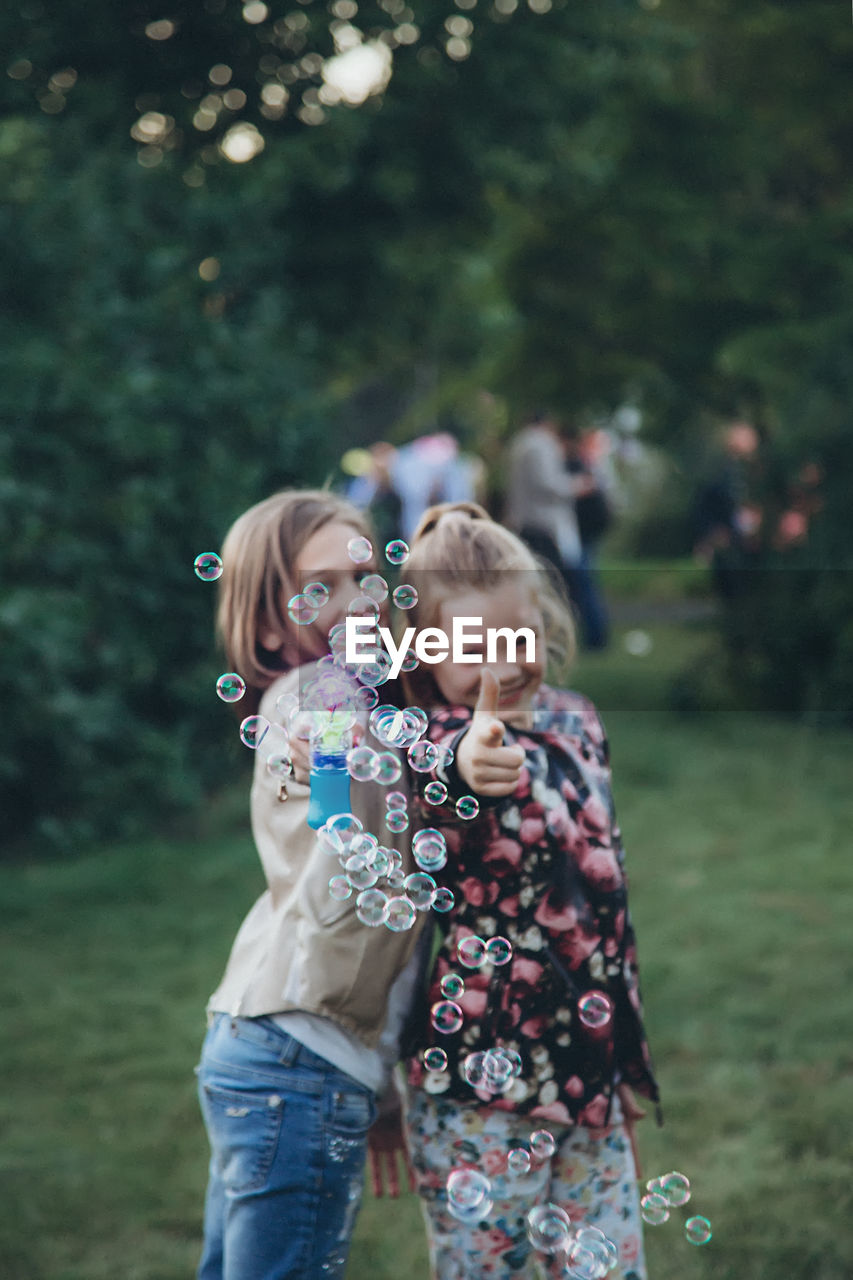 Two girls standing in the park and blowing soap bubbles
