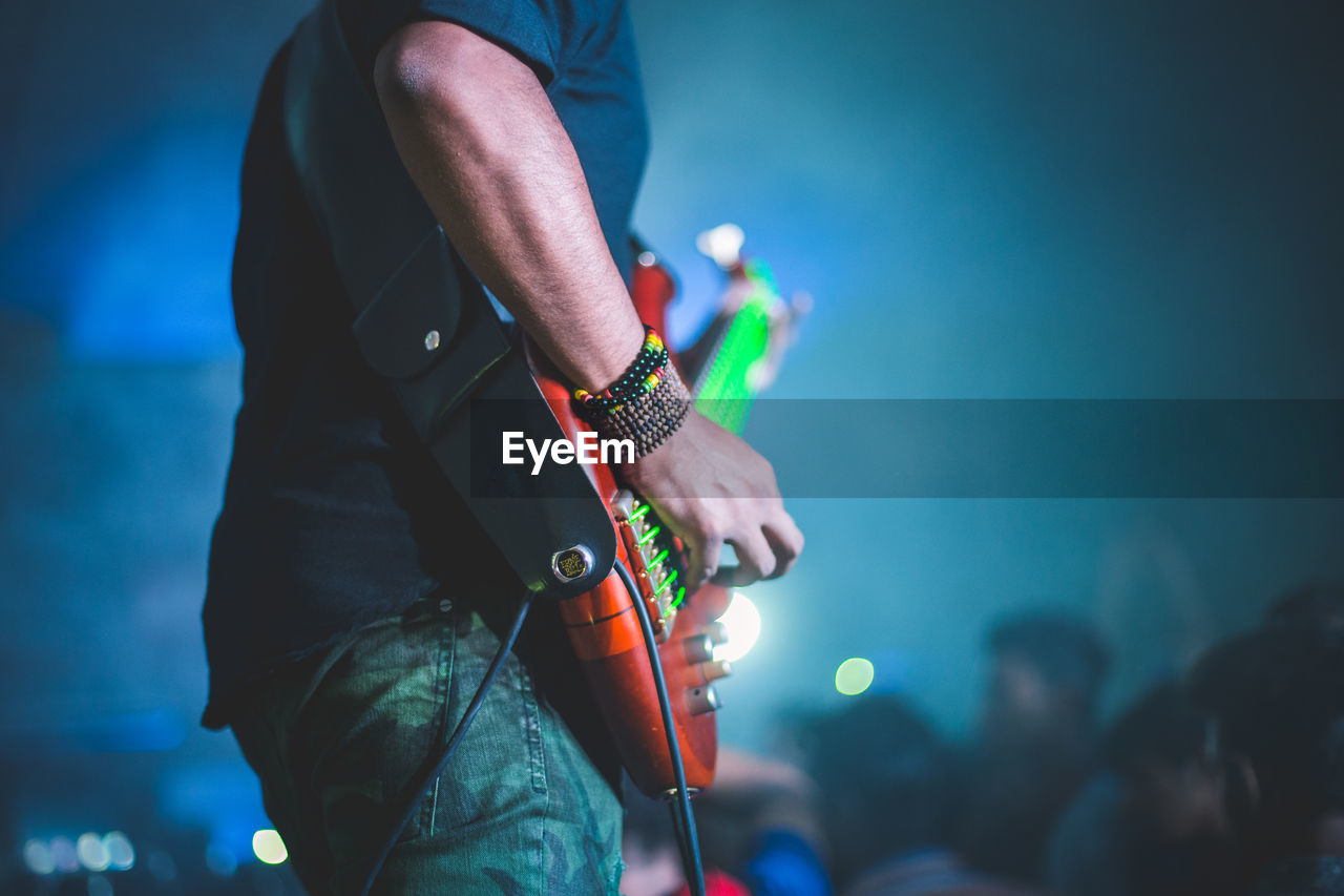 Midsection of man playing guitar while standing on stage