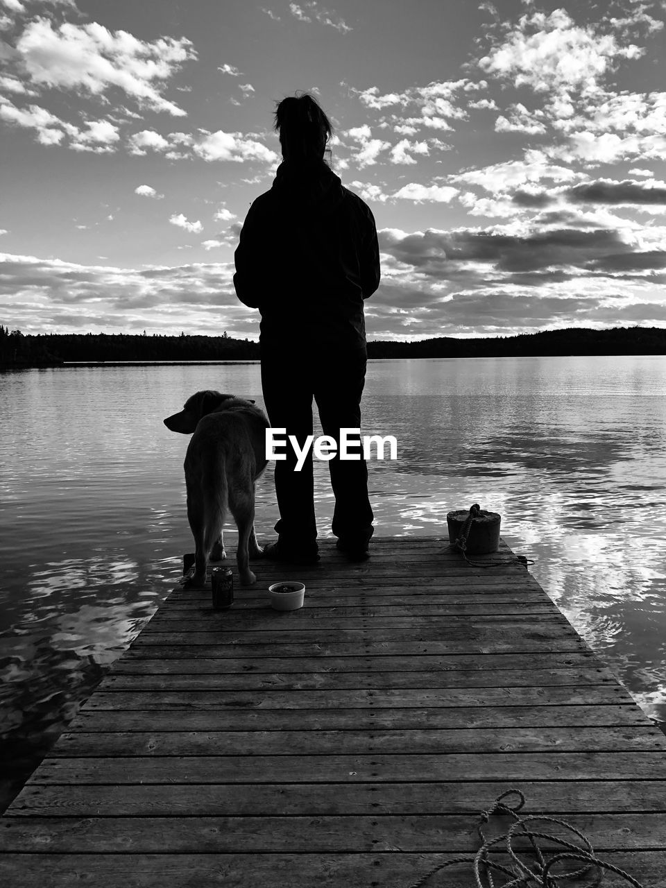 REAR VIEW OF MAN WITH DOG STANDING ON PIER AT SUNSET