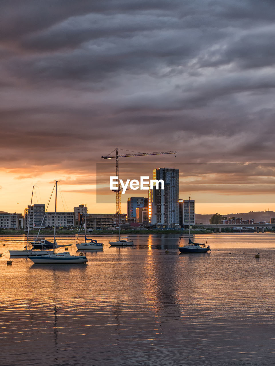 Boats moored in sea by city against cloudy sky during sunset