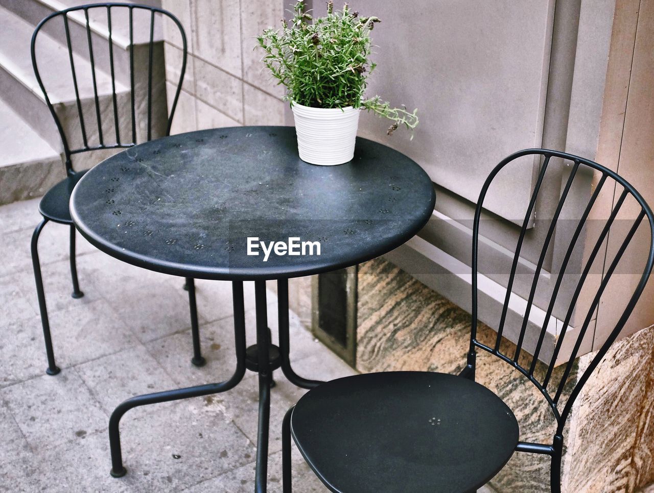 Empty chairs and table on sidewalk by wall