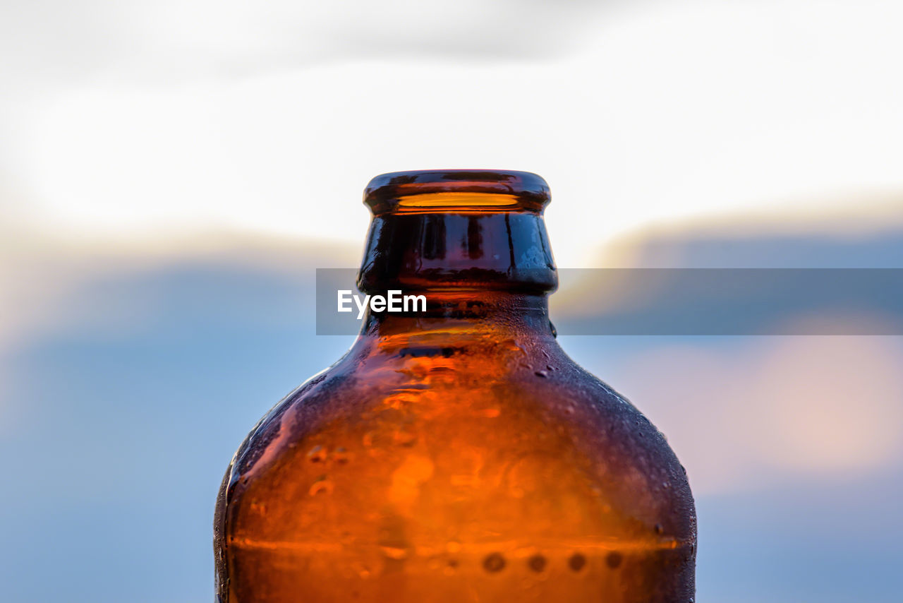 Close-up of water drops on beer bottle against evening sky