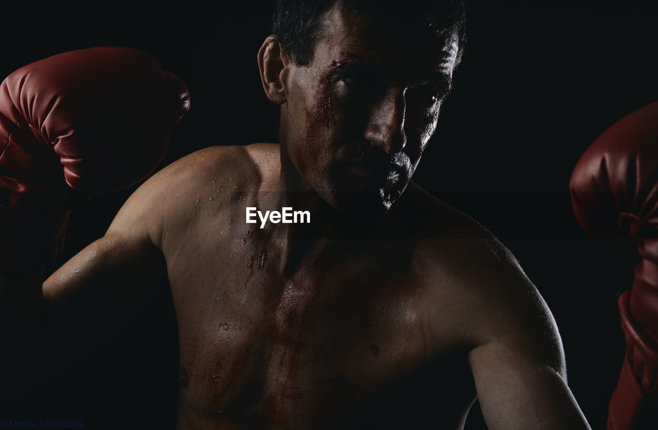  shirtless man with boxing glove standing against black background