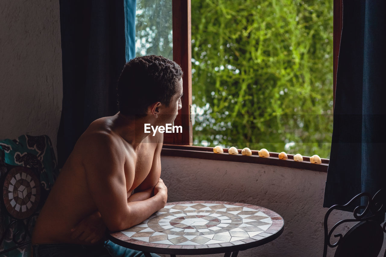 Young man looking through window at home