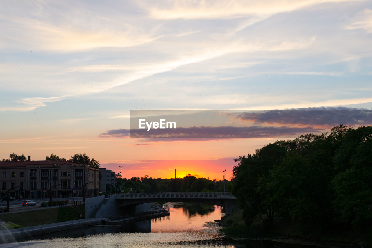 Bridge over river in city against sky at sunset