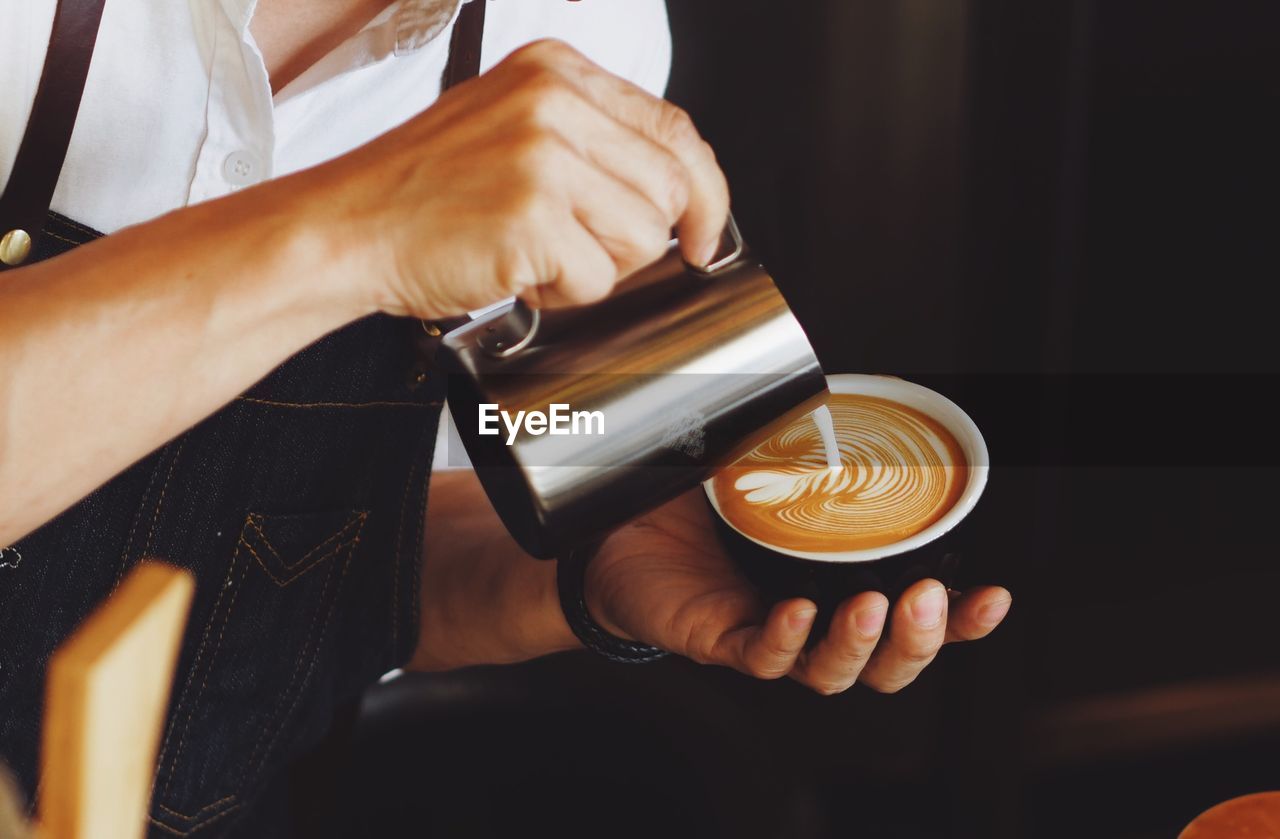 Close-up of hand pouring milk in coffee cup