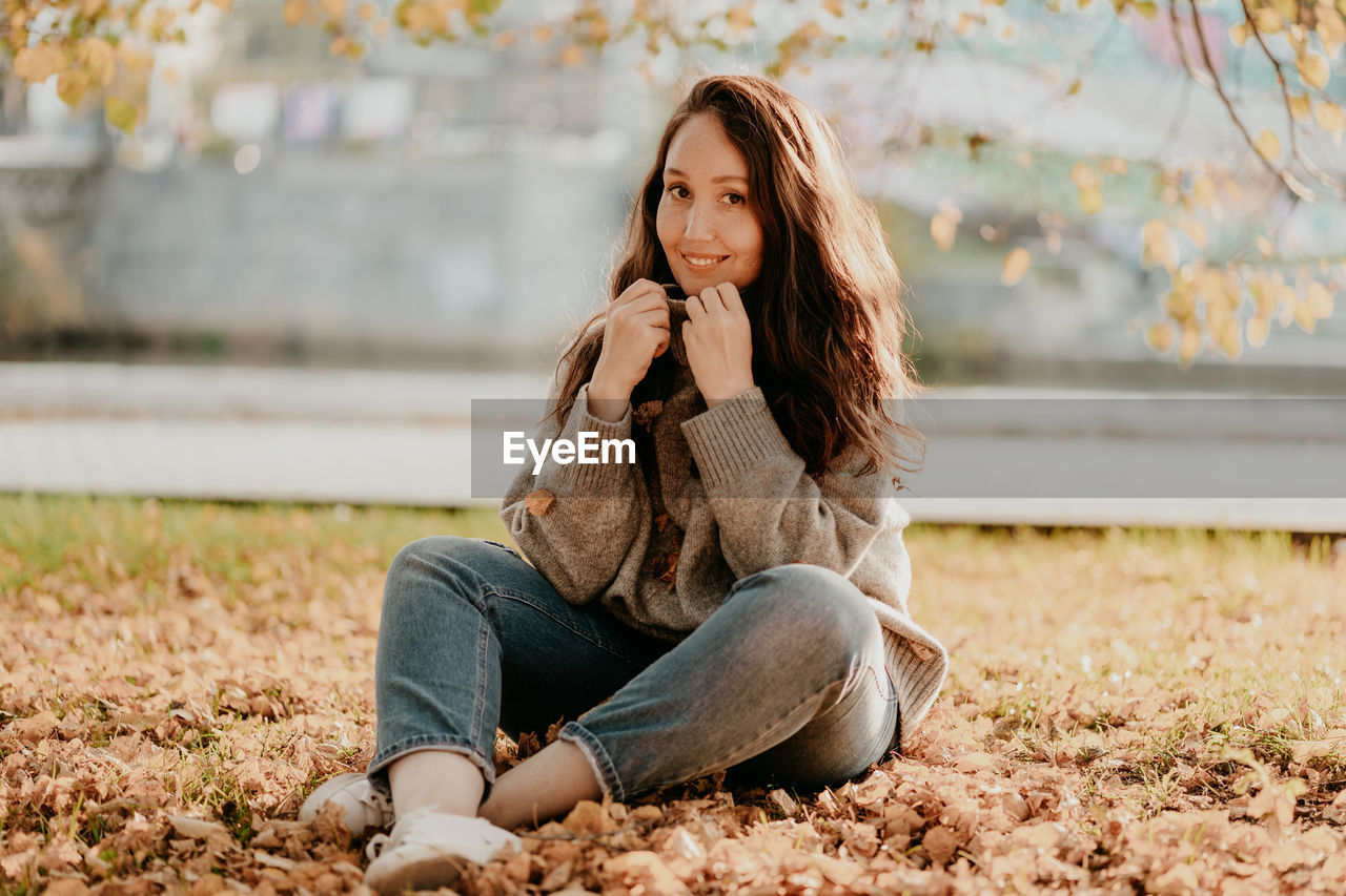 Portrait of woman sitting on grass and dry leaves