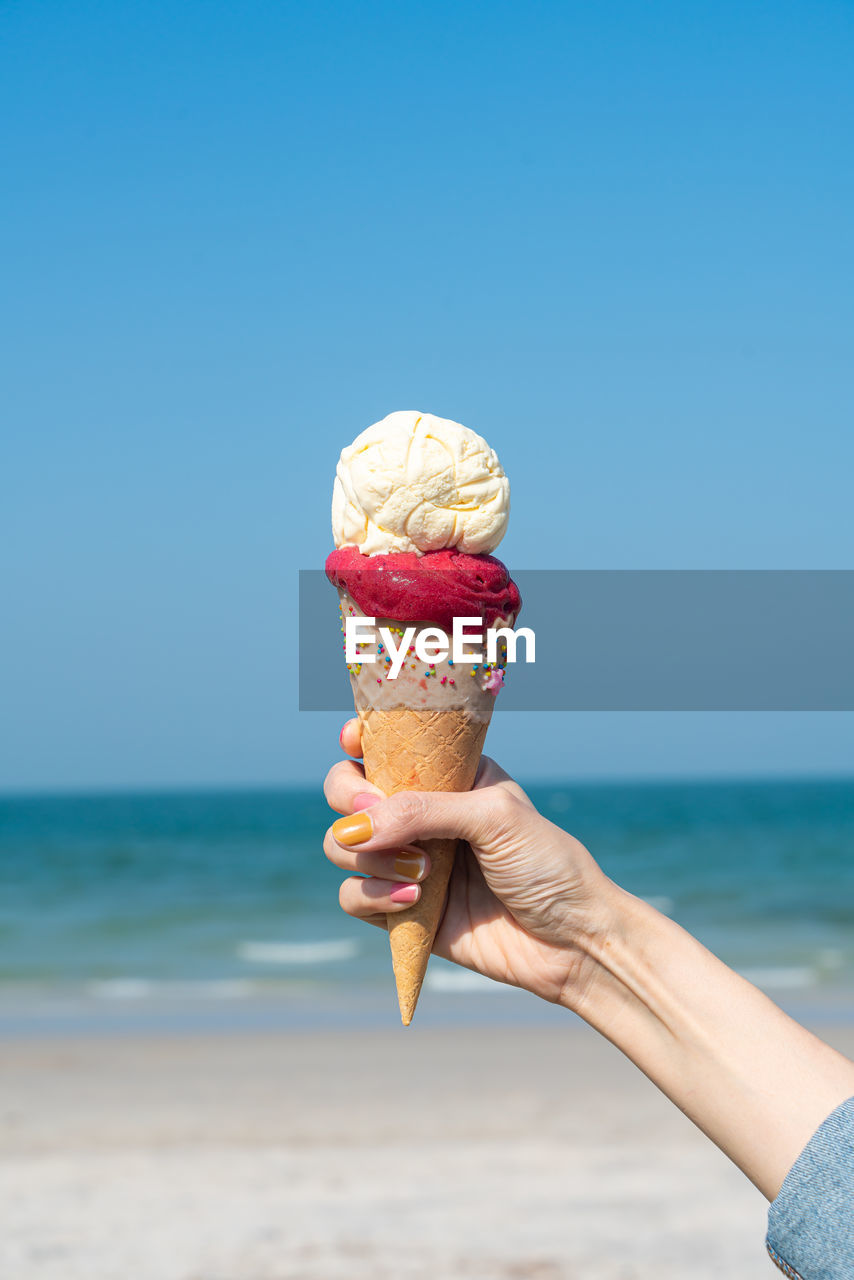 Cropped hand of woman holding ice cream at beach