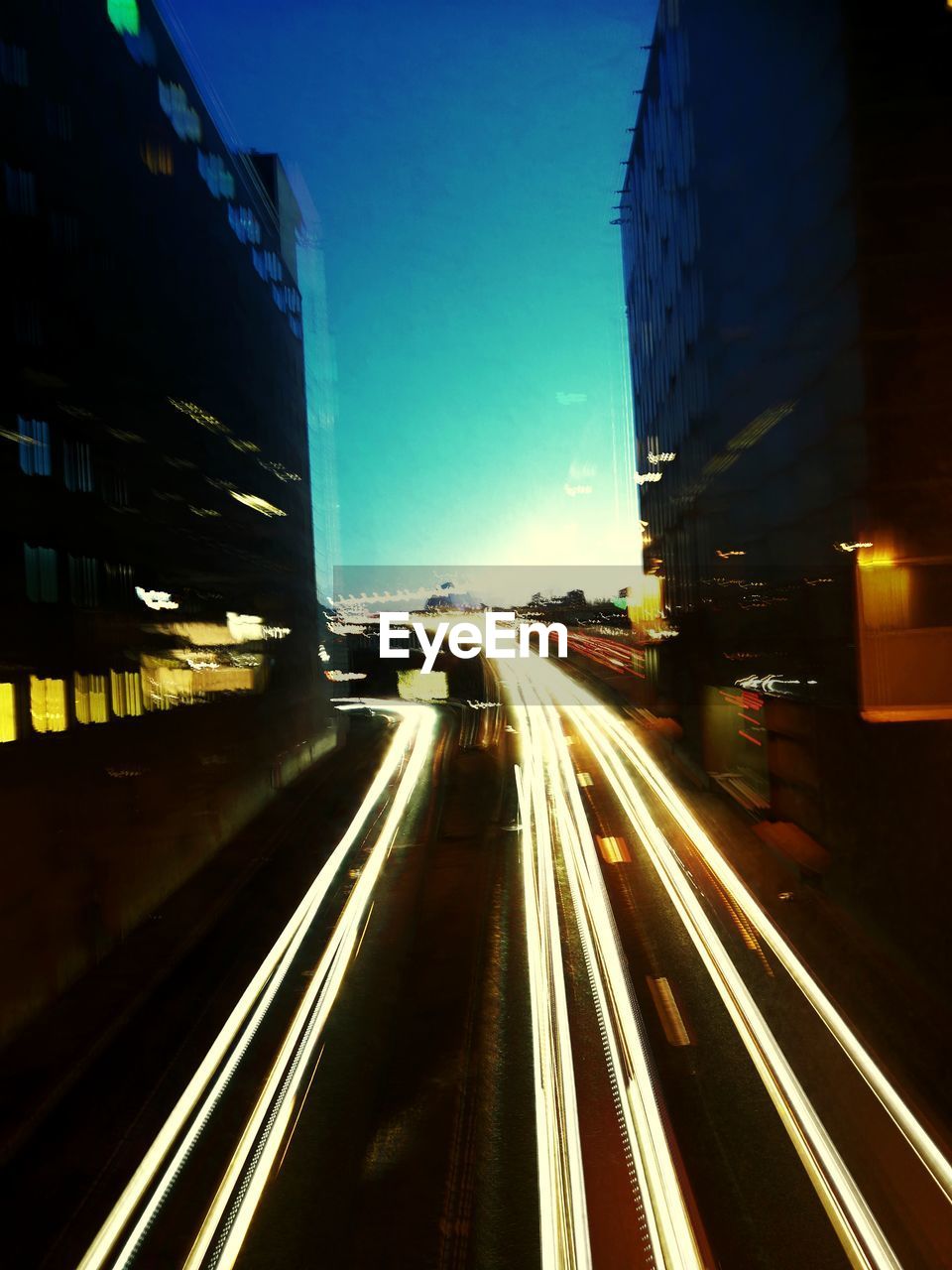 LIGHT TRAILS ON CITY STREET AGAINST SKY AT NIGHT