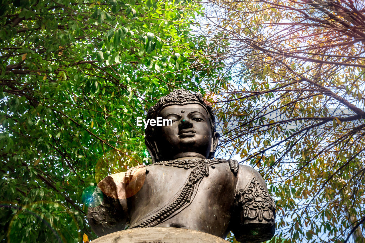 LOW ANGLE VIEW OF FEMALE STATUE AGAINST TREES