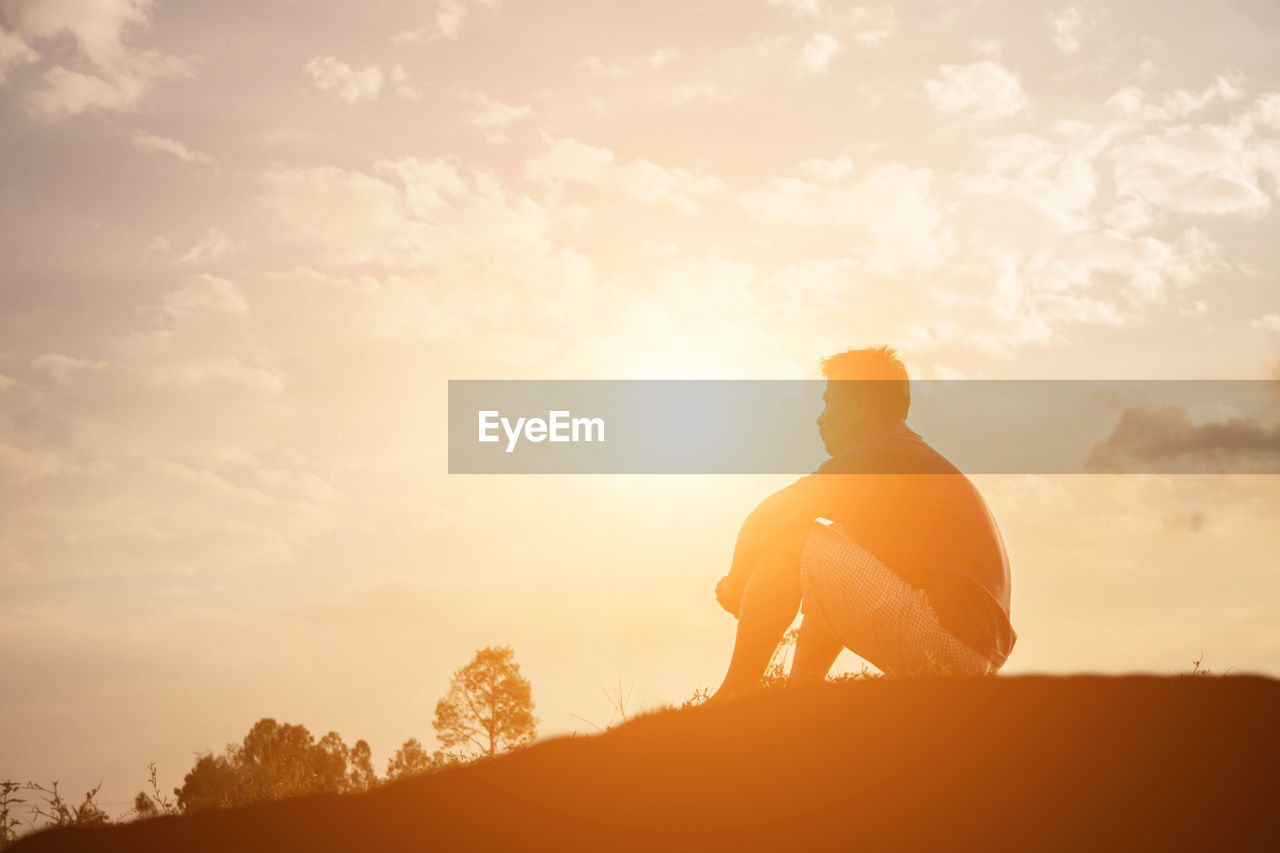 Side view of silhouette man sitting against sky during sunset