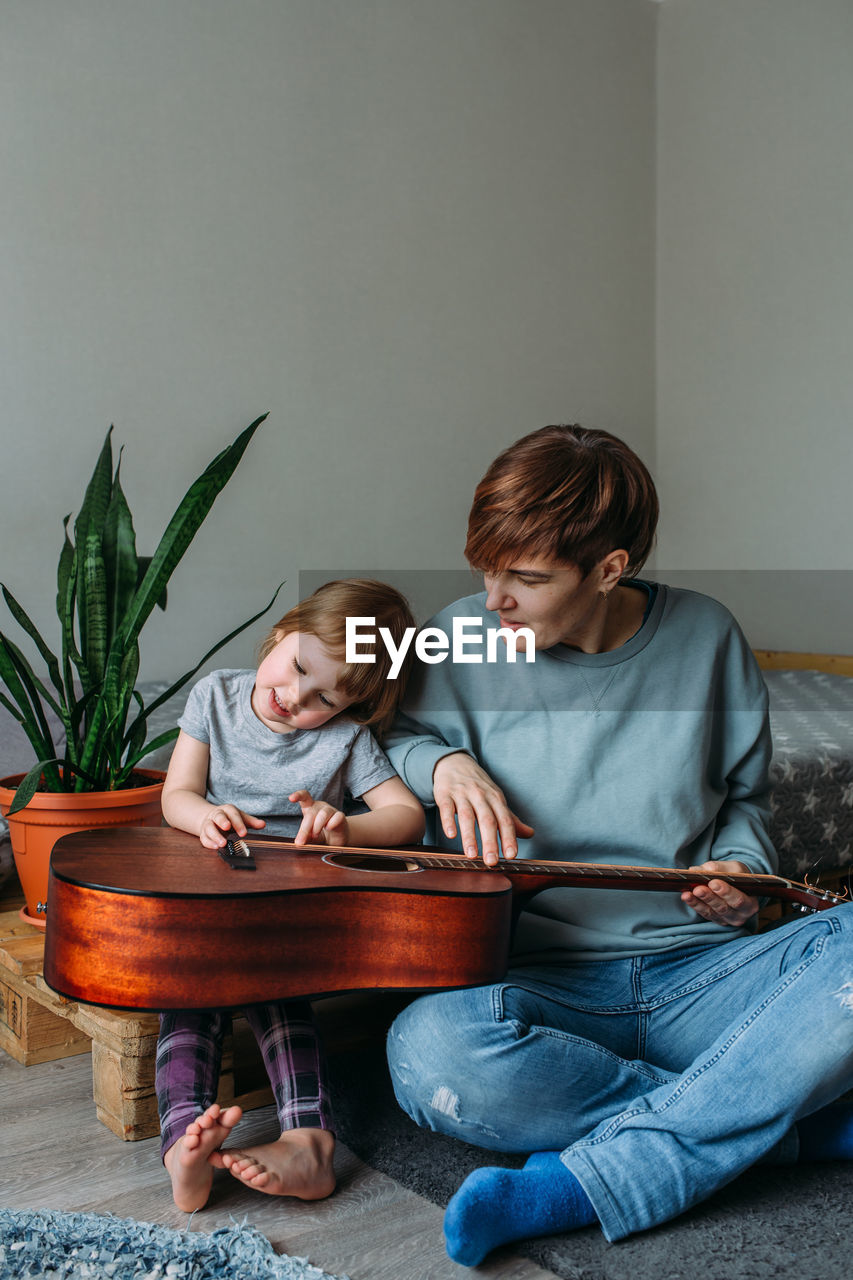 Little girl plays the guitar with her mother on the floor at home