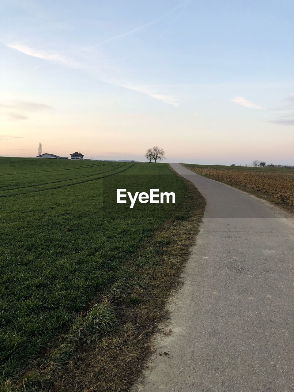 Road amidst field against sky during sunset