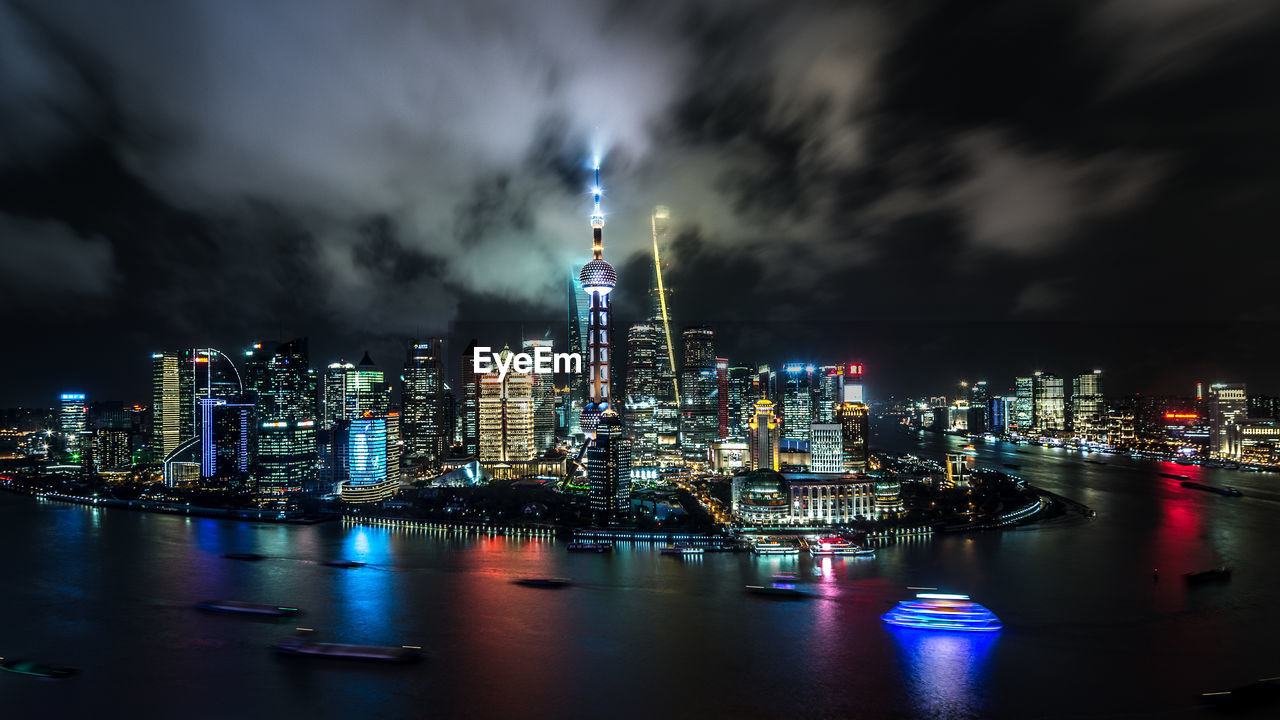 Illuminated buildings by river in city at night