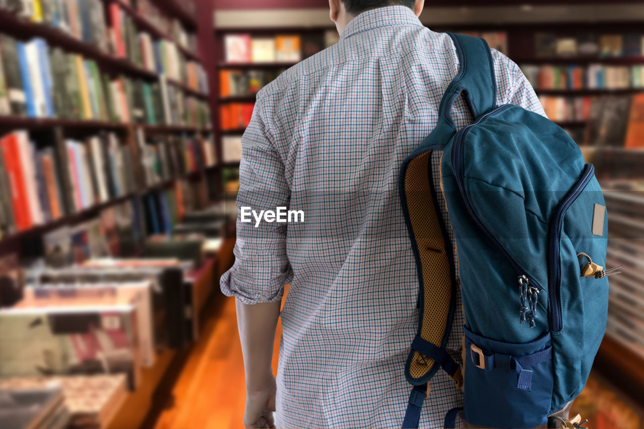 Rear view of man with backpack walking in library