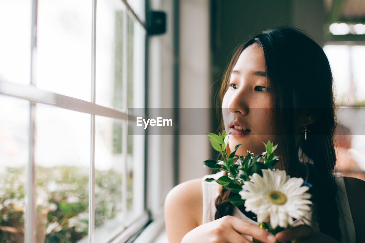 Close-up of woman with flower looking towards window at home